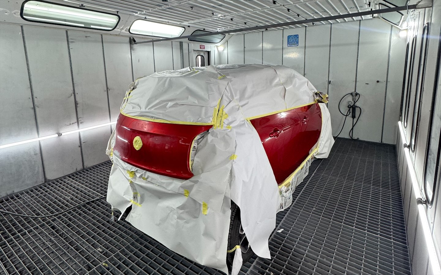Auto rojo cubierto y encintado dentro de la cabina de pintura